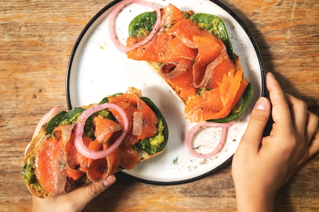 Weibliche Hände und köstliche Toasts mit geräuchertem Lachs, Avocado und Basilikumblättern