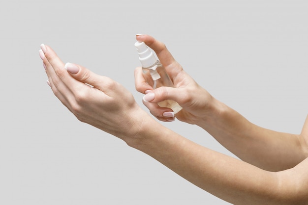 Weibliche Hände unter Verwendung des Händedesinfektionssprayspenders über hellgrauer Wand