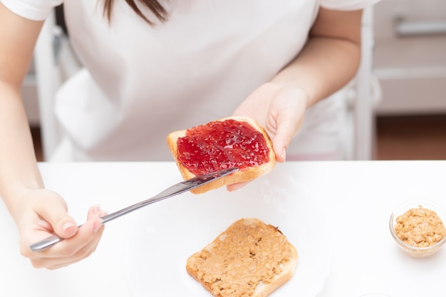 Weibliche Hände verteilen Himbeermarmelade auf Brot