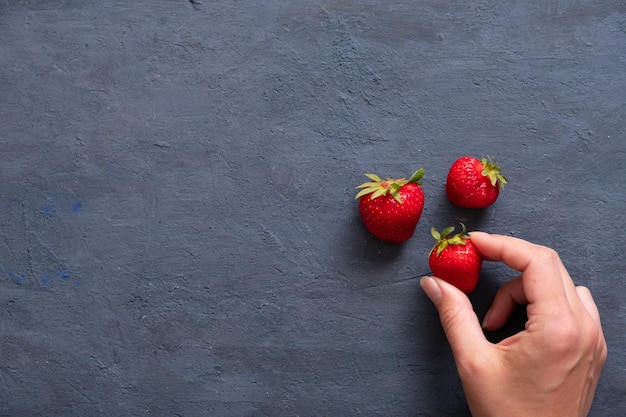 Weibliche Hand breitet drei Erdbeeren auf einem dunklen Steintisch aus