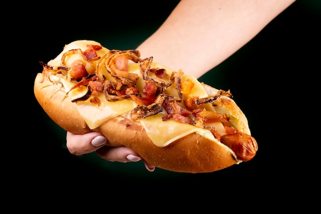 Weibliche Hand, die amerikanischen Hot Dog mit Speck und knusprigen Zwiebeln und geschmolzenem Käse zeigt