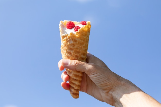 Weibliche Hand, die an einem heißen Sommertag vor blauem Himmelshintergrund handgemachtes Eis in Waffelkegel hält