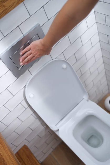 Weibliche Hand, die den Knopf für die Toilettenspülung in der Toiletten-Nahaufnahme drückt