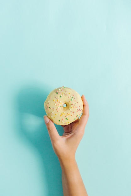 Weibliche Hand, die Donut auf Blau hält.