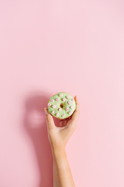 Weibliche Hand, die Donut auf Rosa hält