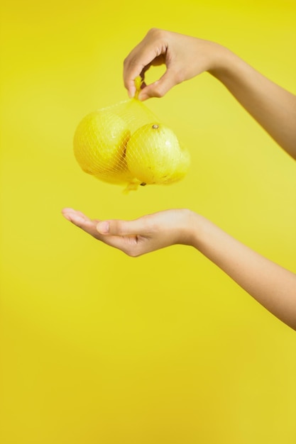 Weibliche Hand, die ein Bündel Zitronen auf gelbem Hintergrund hält Gesunder Lebensstil und Ernährungskonzept