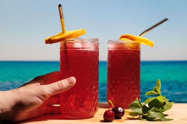 Weibliche Hand, die ein Glas Beerencocktail am tropischen Strand hält