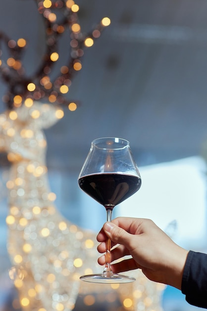 Weibliche Hand, die ein Glas Champagner vor dem Hintergrund eines Weihnachtsbaums hält, der C...