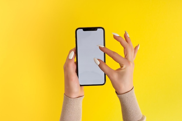 Weibliche Hand, die ein mobiles Smartphone mit weißem Bildschirm hält und berührt, isoliert auf gelb Fotovorlage für alle Bilder auf dem Handy-Display Layout mit leicht entfernbarem Hintergrund des Telefonmonitors