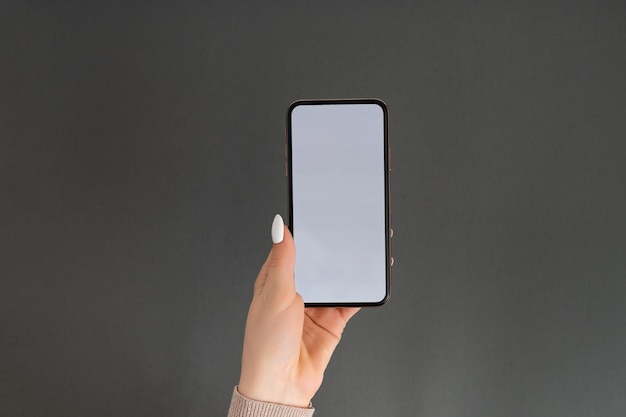 Weibliche Hand, die ein mobiles Smartphone mit weißem Bildschirm hält und berührt, isoliert auf grau Fotovorlage für alle Bilder auf dem Handy-Display Layout mit leicht entfernbarem Hintergrund des Telefonmonitors