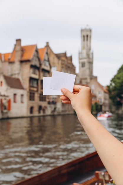 Weibliche Hand, die ein Ticket oder eine Visitenkarte mit Kopienraum auf dem Hintergrund eines Kanals und mittelalterlicher Häuser in Brügge Belgien hält