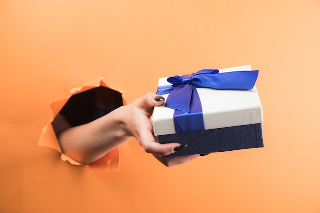 Weibliche Hand, die eine Geschenkbox auf einem orangefarbenen Hintergrund hält