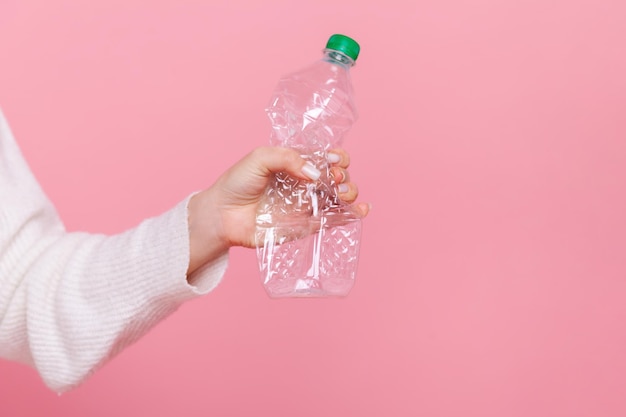 Weibliche Hand, die eine Plastikflasche mit grüner Kappe hält, die ihren Müll sortiert und sich Sorgen um die Umwelt macht