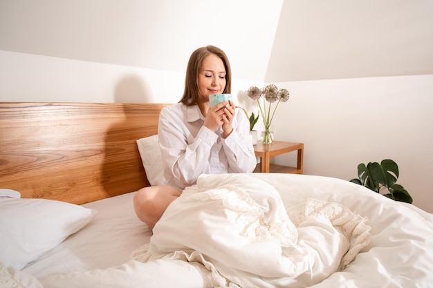 Weibliche Hand, die eine Tasse Kaffee hält, während sie im Bett sitzt