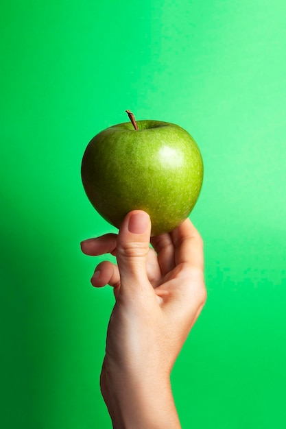 Weibliche Hand, die einen grünen Apfel mit grünem Hintergrund und Kopienraum hält