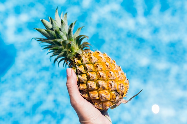 weibliche Hand, die frische Ananas im Swimmingpool im Hotel hält.