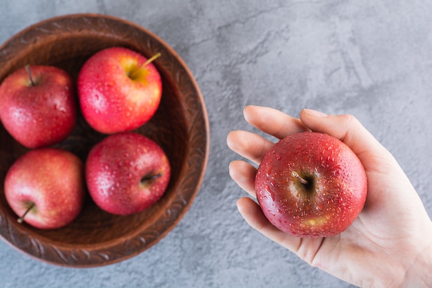 Weibliche Hand, die frischen roten Apfel auf grau hält.