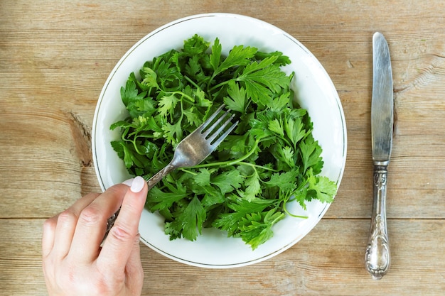 weibliche hand, die grünen kräutersalat vom alten holztisch des plateons isst
