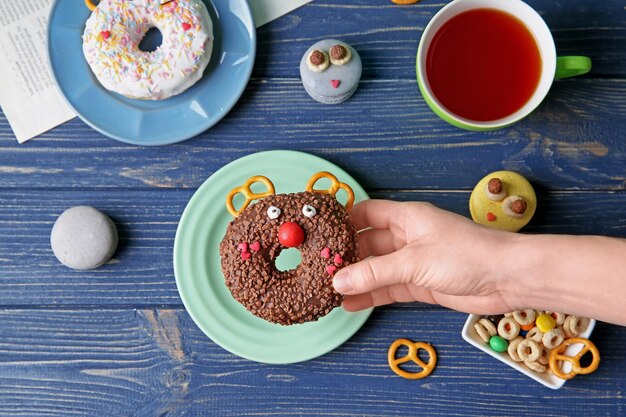 Weibliche Hand, die kreativen Donut auf hölzernem Hintergrund hält