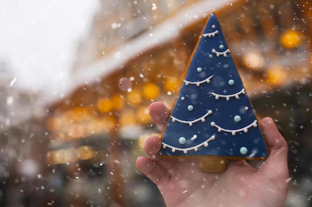 Weibliche Hand, die leckeres Ingwerplätzchen am Feiertagsweihnachtsmarkt hält. Hintergrund mit verschwommenen Bokeh-Lichtern