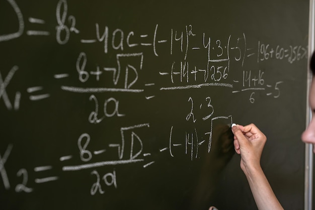 Weibliche Hand, die mathematische Formeln auf der Klassentafel schreibt