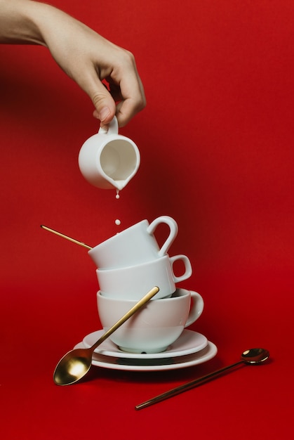 Weibliche Hand, die Milchglas hält und in Stapel weiße Kaffeetassen gießt