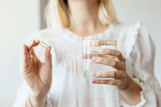 Weibliche hand, die omega 3-fischölergänzungskapsel und -glas wasser hält