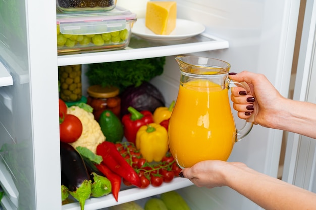 Weibliche Hand, die Orangensaftglas von einem Kühlschrank nah oben nimmt