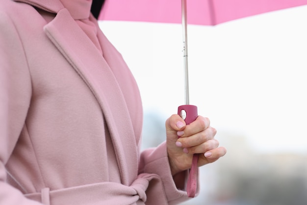 Weibliche Hand, die rosa Regenschirm in der Regennahaufnahme hält. Wettervorhersagekonzept