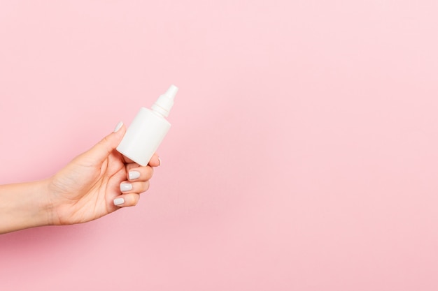 Weibliche Hand, die Sahneflasche Lotion lokalisiert hält. Mädchen geben kosmetische Produkte des Gefäßes auf Rosa