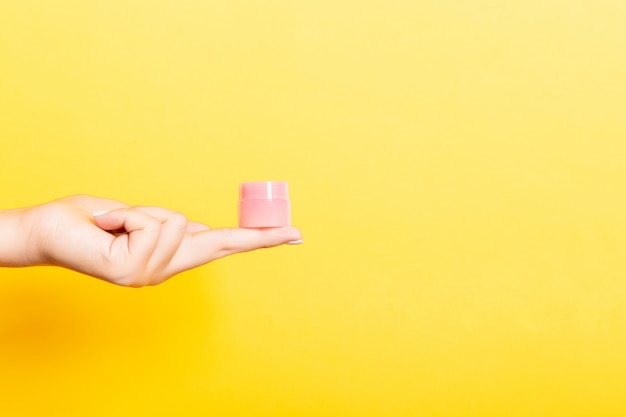 Weibliche Hand, die Sahneflasche Lotion lokalisiert hält. Mädchen geben kosmetische Produkte des Glases auf Gelb