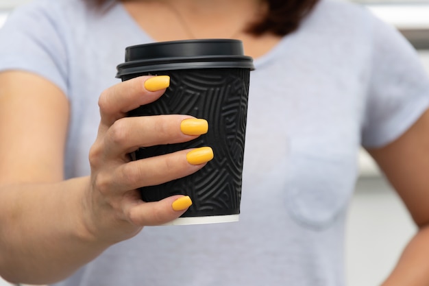 Weibliche Hand, die schwarze Papierschale mit Kaffee zum Mitnehmen hält