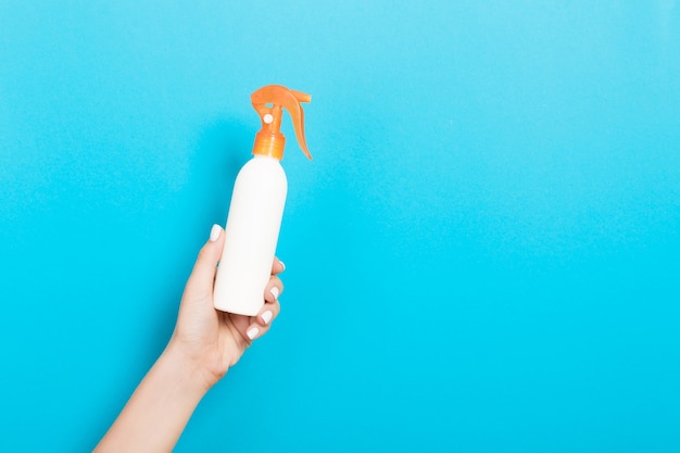 Weibliche Hand, die Sprühcremeflasche Lotion lokalisiert hält. Mädchen geben kosmetische Produkte auf blauem Hintergrund.