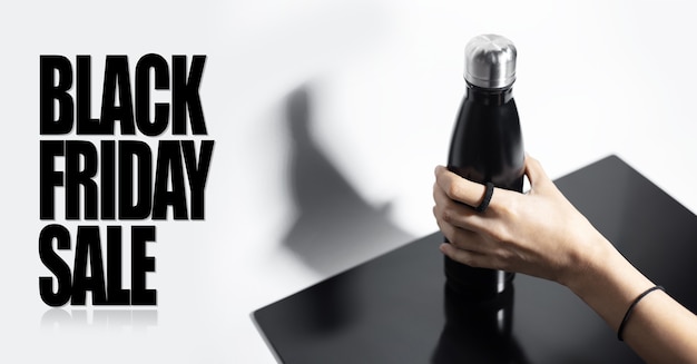 Weibliche Hand, die Stahlthermowasserflasche nahe Text des Black Friday-Verkaufs hält. Hintergrund der weißen Farbe.