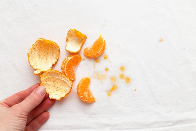 Weibliche Hand, die weiße Kleidung mit Ditryflecken von der Fruchtmandarine hält