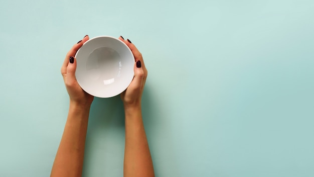 Weibliche Hand, die weiße leere Schüssel auf blauem Hintergrund mit Kopienraum hält.