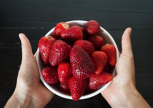 Weibliche Hand, die weiße Schüssel mit Erdbeeren hält