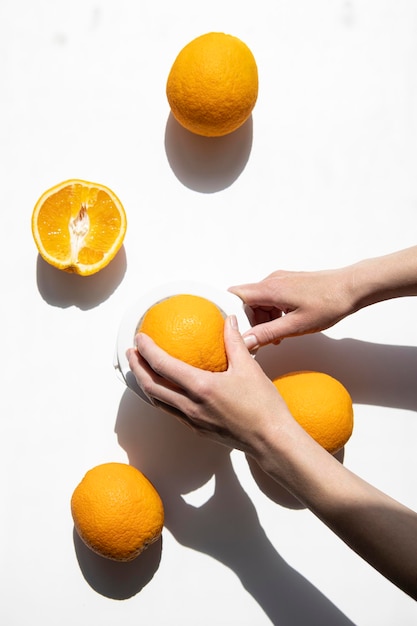 Weibliche Hand drückt Saft aus Orangen in einer Handschüssel auf weißem Hintergrund Draufsicht flach liegend