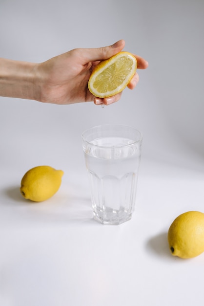 Weibliche Hand drückt Zitronensaft in ein Glas Wasser.