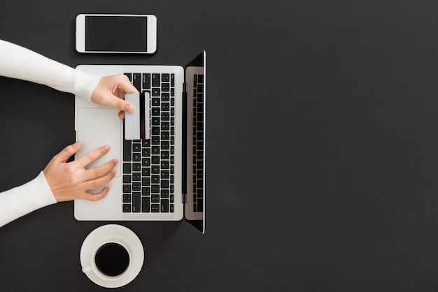 Weibliche Hand fügt Daten in das Notebook ein und hält Kreditkarte