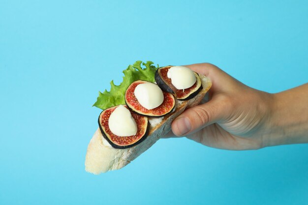 Weibliche Hand hält Bruschetta mit Feige auf blauem Hintergrund