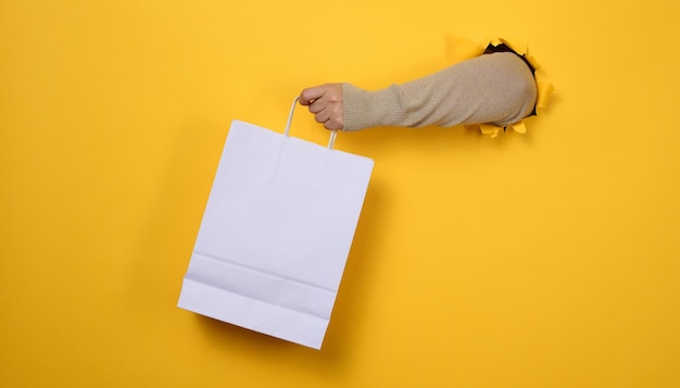 Weibliche Hand hält eine Einwegtüte aus weißem Papier mit Griffen für Lebensmittel und Kleidung. Recycelbare Verpackung. Kein Verlust. Verkauf