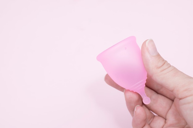 Weibliche Hand hält eine Menstruationstasse über rosa Wand, Kopierraum. Frauengesundheitskonzept, Alternative zu Plastikmüll, Null-Abfall-Konzept