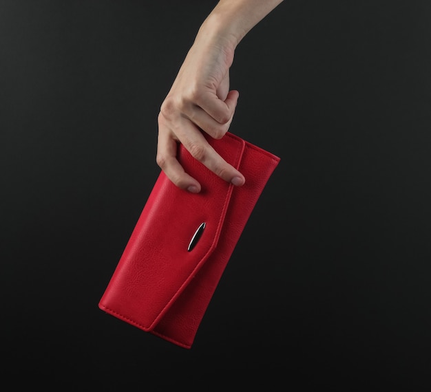 Weibliche Hand hält eine rote Lederhandtasche auf einem schwarzen Hintergrund