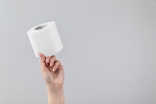 Weibliche Hand hält eine weiche Rolle Toilettenpapier auf grauem Hintergrund