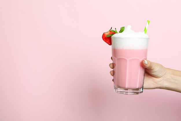 Weibliche Hand hält Glas Erdbeermilchshake auf rosa Hintergrund