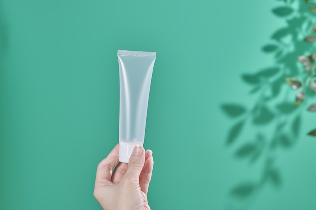 Weibliche Hand hält kosmetisches Produkt in Röhrenglasflasche Lotion Anti-Aging-Feuchtigkeitscreme ätherisches Öl oder Serum für das Gesicht auf grünem Hintergrund mit heller Schattennatur Schönheit kosmetisches Hautpflegekonzept