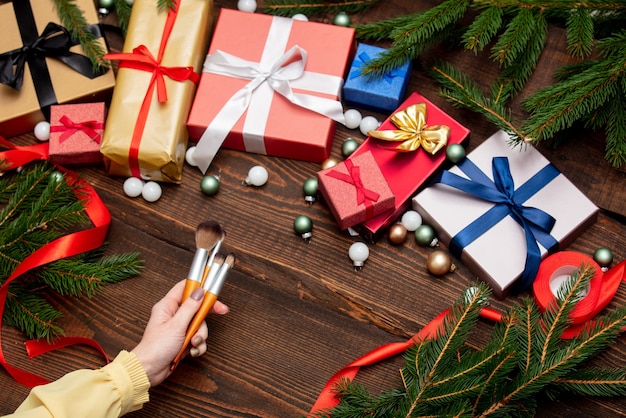 Weibliche Hand hält Make-up-Pinsel nahe Weihnachtsgeschenken