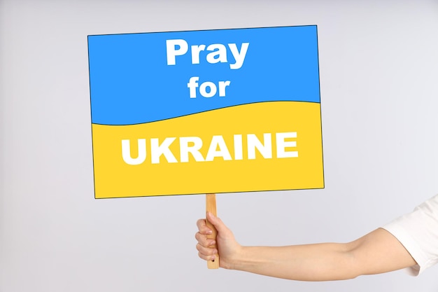 Weibliche Hand hält Protestschild mit Text Pray for Ukraine