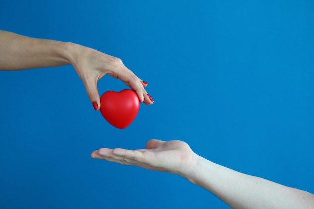 Weibliche Hand hält rotes Herz und überträgt es auf männliche Hand.